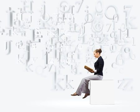 Young attractive businesswoman sitting on white cube and readingの写真素材