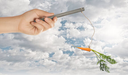Close up of hand holding stick with carrot dangling on ropeの写真素材