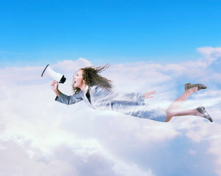 Young businesswoman with megaphone flying high in skyの写真素材