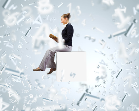Young attractive businesswoman sitting on white cube and readingの写真素材