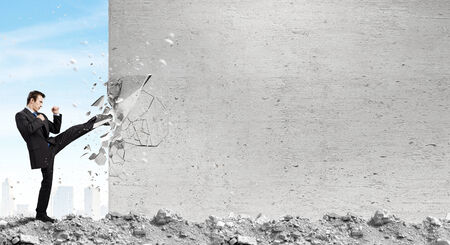 Businessman breaking stone wall with karate kickの写真素材