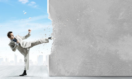 Businessman breaking stone wall with karate kick