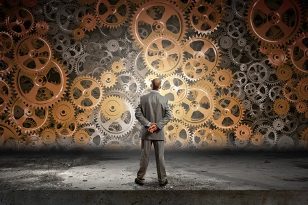 Back view of businessman looking at mechanism of cogwheelsの写真素材