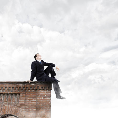 Young businessman sitting on roof of buildingの写真素材