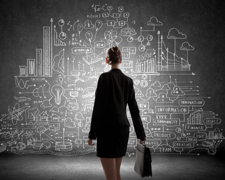 Rear view of businesswoman looking at business sketches on wallの写真素材