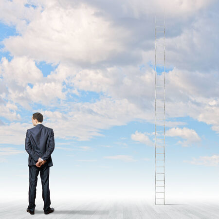 Rear view of businessman standing near ladder going high in skyの写真素材