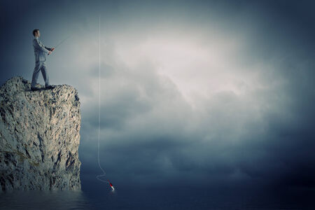 Businessman sitting on rock and fishing with rodの写真素材