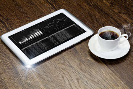 Tablet pc cup of coffee and notepad at tableの写真素材