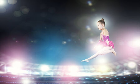 Cute girl gymnast in performance costume jumping highの写真素材