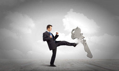 Angry businessman crashing stone key with punchの写真素材