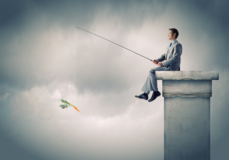 Businessman sitting on top of building and fishing with rodの写真素材
