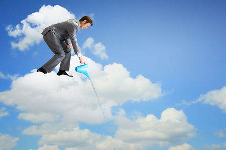 Young businessman standing on cloud and watering something belowの写真素材