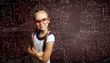 Little cute girl of school age in glasses against blackboardの写真素材