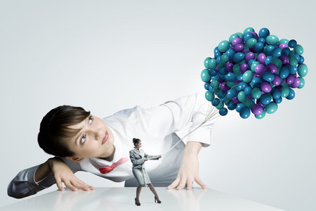 Businesswoman looking at businesswoman miniature pulling bunch of balloonsの写真素材