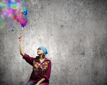 Young woman painter with brush and colorful splashes aboveの写真素材