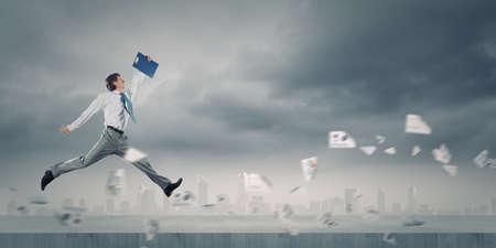 Young cheerful businessman in jump against city backgroundの写真素材