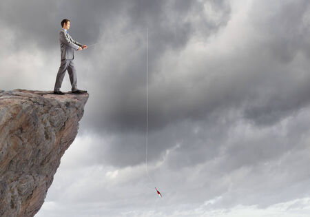 Businessman sitting on rock and fishing with rodの写真素材