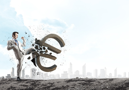 Businessman breaking stone euro symbol with karate punchの写真素材