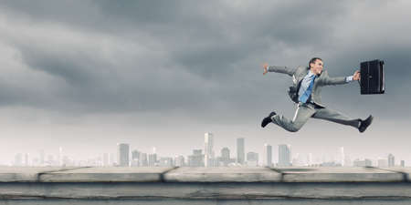 Young cheerful businessman in jump against city backgroundの写真素材