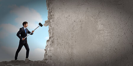 Young determined businessman with hammer in handsの写真素材