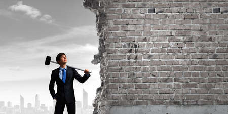 Young determined businessman with hammer in handsの写真素材