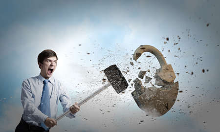 Young angry businessman crashing stone lock with hammerの写真素材