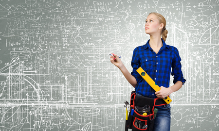 Young woman mechanic with ruler in hand against city backgroundの写真素材