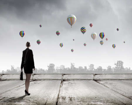 Rear view of businesswoman looking at aerostats flying above cityの写真素材