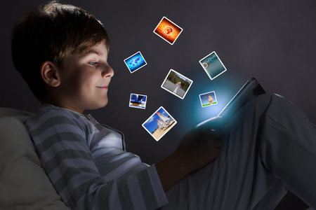 Cute little boy sitting in bed and using tablet pcの写真素材