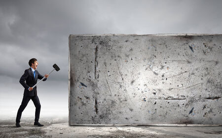 Young determined businessman with hammer in handsの写真素材