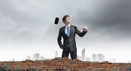 Young determined businessman with hammer in handsの写真素材