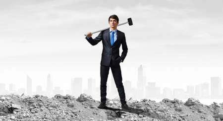 Young determined businessman with hammer in handsの写真素材