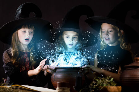 Three little Halloween witches reading spell above potの写真素材