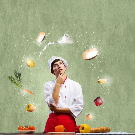 Young thoughtful cook and ingredients flying in airの写真素材