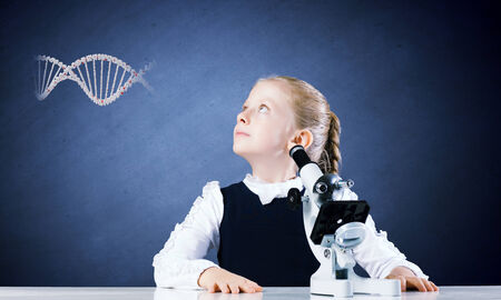 Cute school girl with microscope against blackboardの写真素材