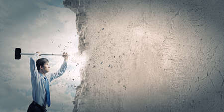 Young determined businessman with hammer in handsの写真素材