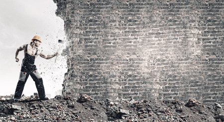 Strong man in uniform breaking brick wall with hammerの写真素材