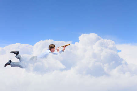 Young businessman flying in sky and lokking in spyglassの写真素材