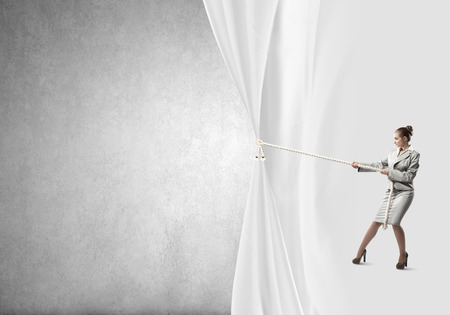Young businesswoman pulling curtain with rope  Place for textの写真素材