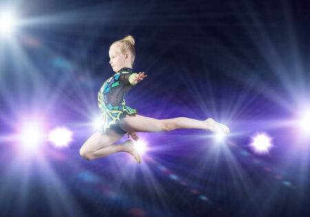 Cute girl gymnast in performance costume jumping highの写真素材
