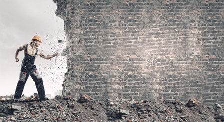 Strong man in uniform breaking brick wall with hammerの写真素材
