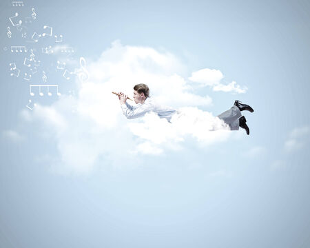 Young businessman flying in sky and playing fifeの写真素材