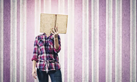 Young woman in casual hiding face behind readingの写真素材