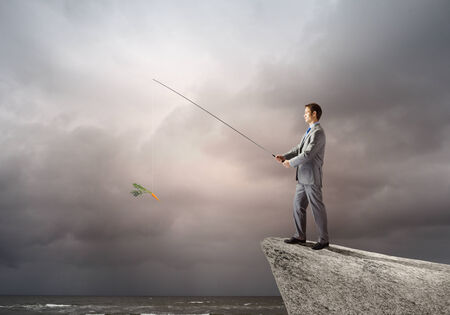 Businessman standing on rock and fishing with rodの写真素材