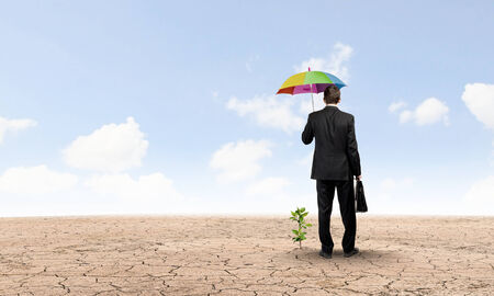 Rear view of businessman protecting little sprout with umbrellaの写真素材