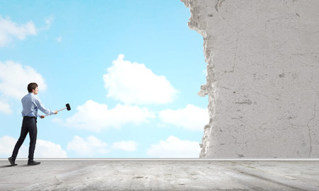 Young determined businessman with hammer in handsの写真素材