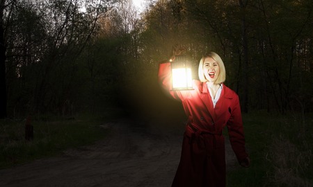 Young woman in red cloak with lantern lost in forestの写真素材