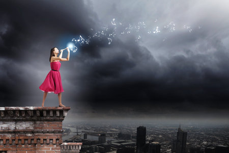 Young woman in red dress on building top playing fifeの写真素材