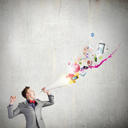 Young businessman speaking in trumpet and colorful icons flying outの写真素材