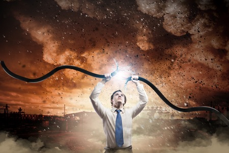 Young businessman tearing electricity cable with handsの写真素材